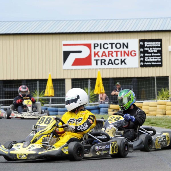 Racers riding around the go-kart track with Picton Karting Track signage in the background