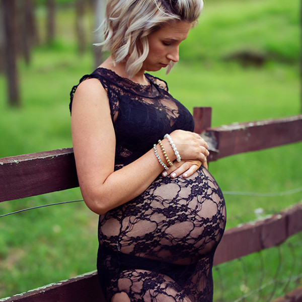 Pregnant lady standing against a fence in a field