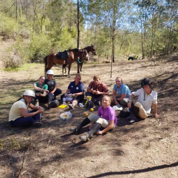 Group of riders sitting down to enjoy lunch in the bush with the horses tied up to a tree