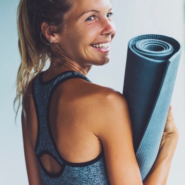Young lady with blonde hair holding her yoga mat and smiling