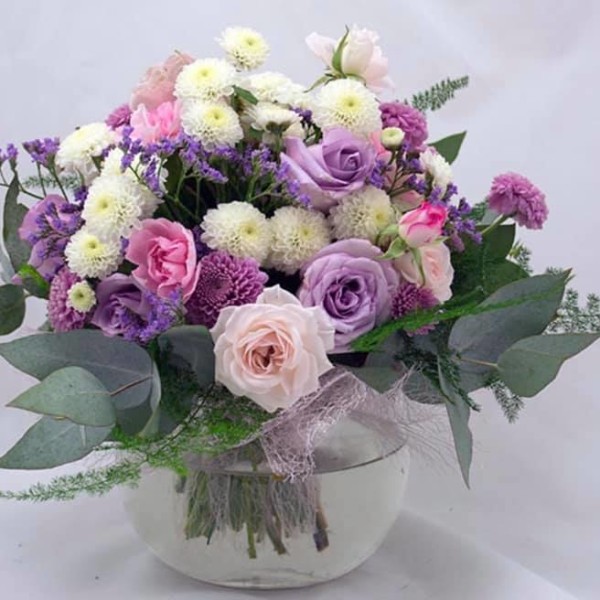 Round glass vase holding a bouquet of purple, pink and white flowers